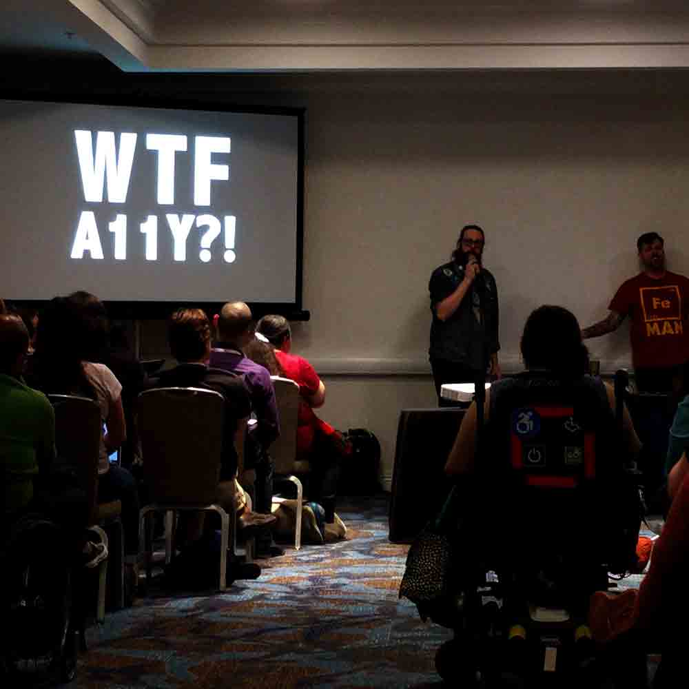 Billy Gregory and Karl Groves standing in front of a project slide that reads “WTF A11y?”