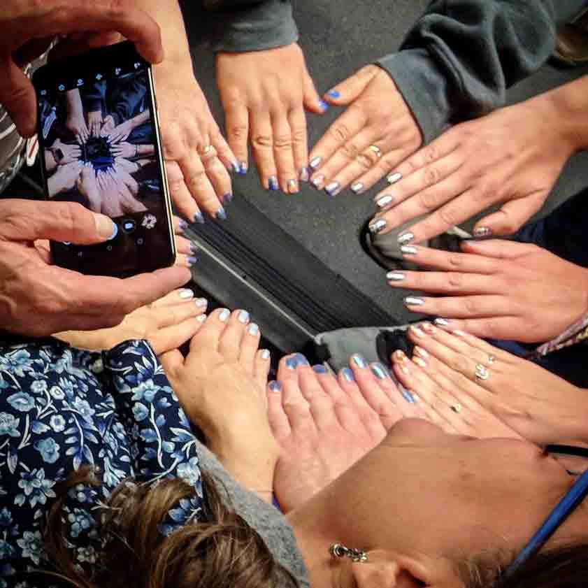A circle of 12 hands all showing their nails to Bruce’s cell phone camera.