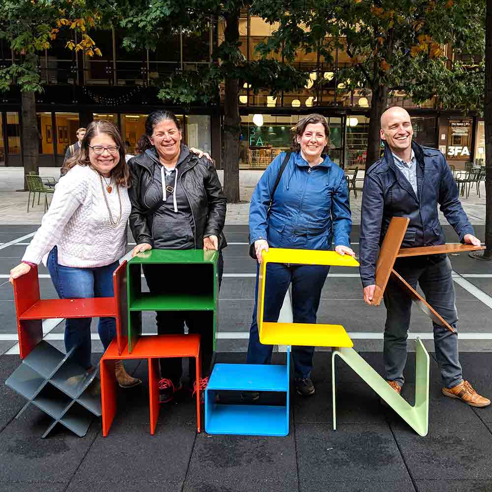 Glenda, Estelle, Janet, and Adrian holding colorful metal letters to spell ‘hack‘ and ‘#mdn’.